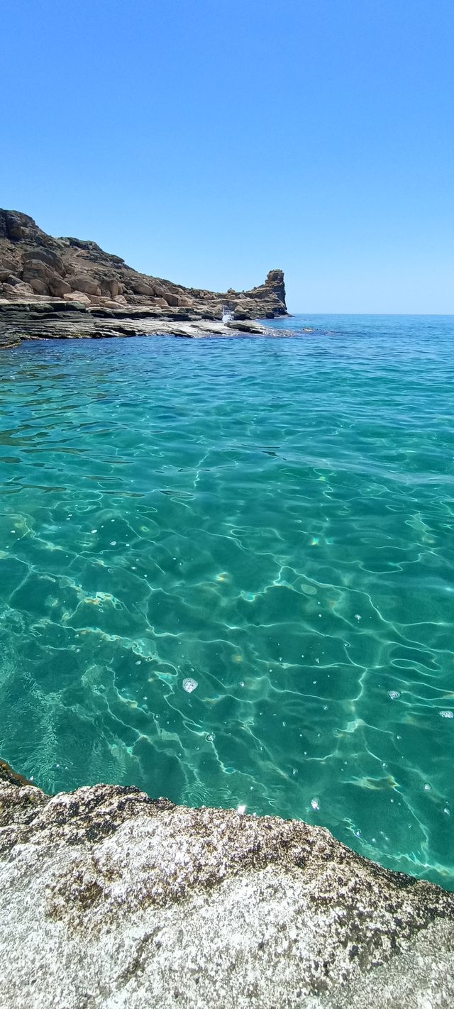 Прозрачная вода Голубой бухты над каменистым дном, у мыса — отдельно стоящий скальный останец.