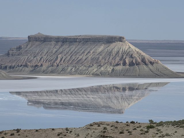 Останец Карынжарыка отражается в разливе солёной воды на дне впадины.