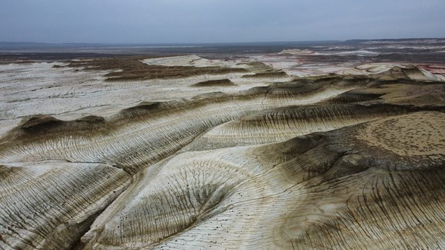 Кызылкуп сверху: волны слоистых гряд уходят к горизонту в пасмурный день.