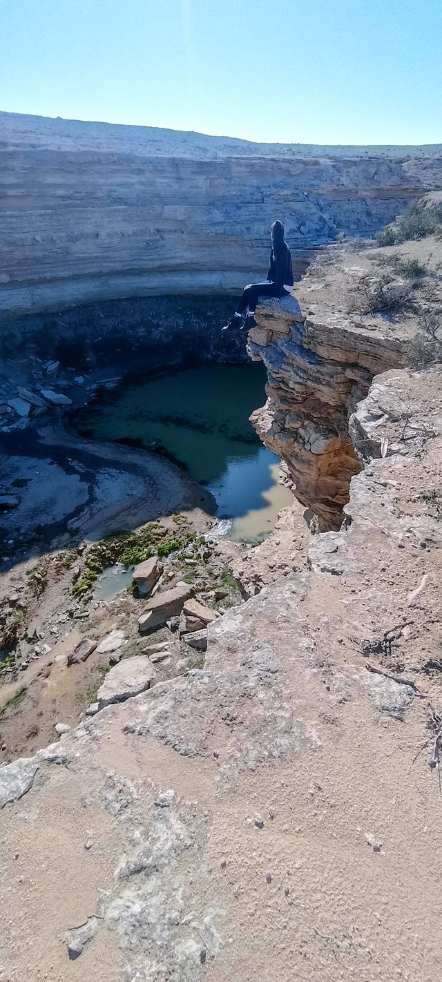 Гостья сидит на скальном выступе над озером Саура, внизу — зелёная вода в каменной чаше.