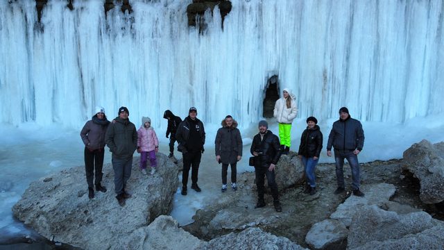 Зимний Тамшалы: группа гостей джип-тура у стены замёрзшего водопада из сосулек.