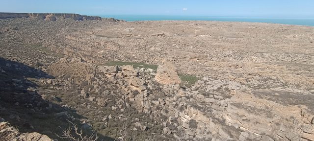 Панорама провала Жыгылган: поле обрушенных глыб спускается к морю, вдали бирюзовая вода.