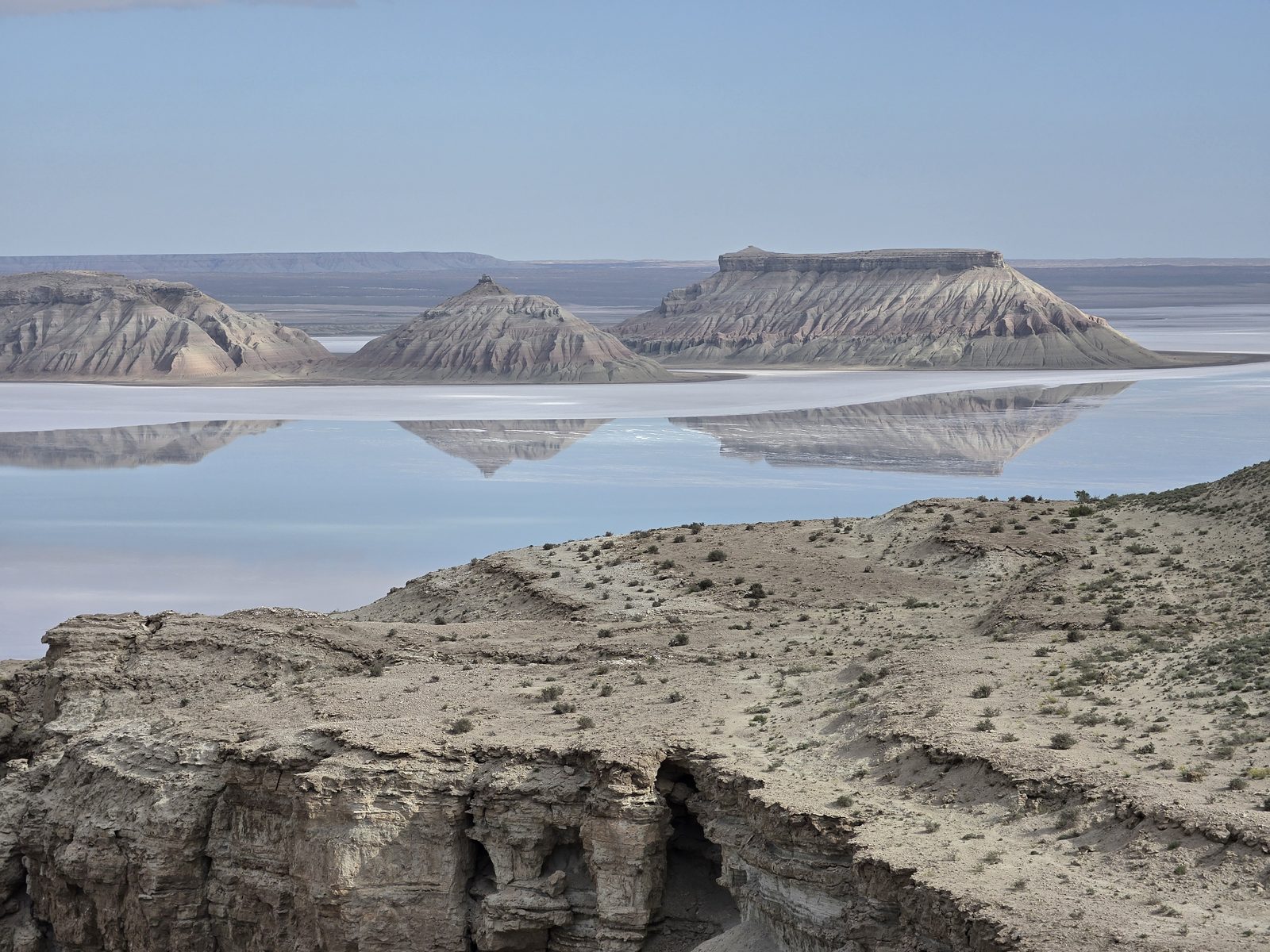 Три останца Карынжарыка отражаются в разливе солёной воды впадины.