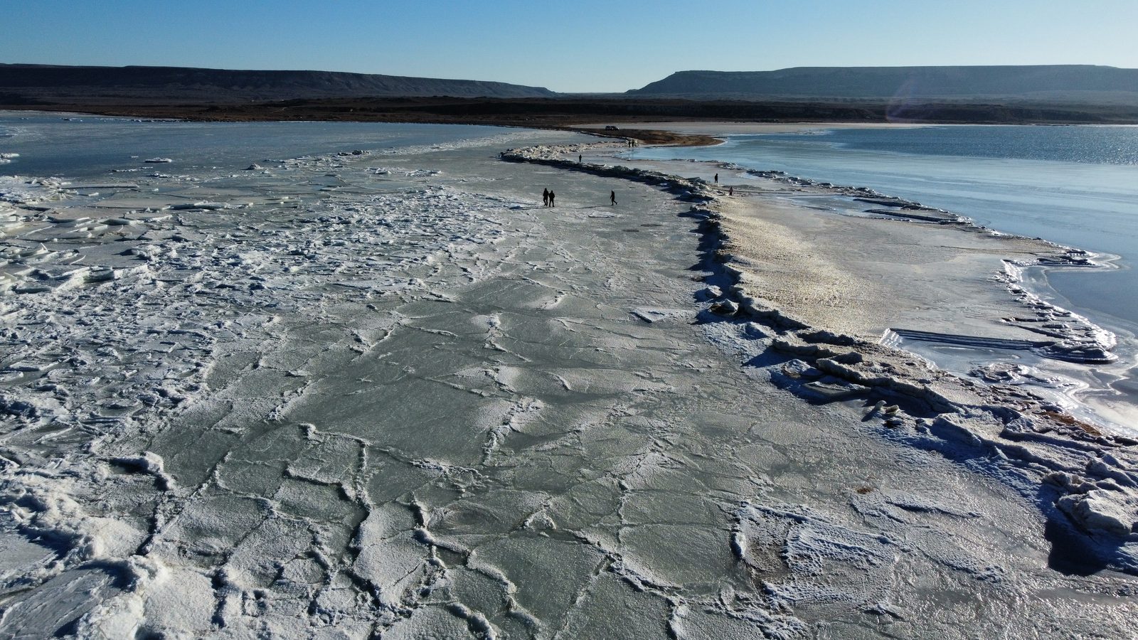 Замёрзшая бухта Каспия: люди идут по ледяному полю к открытой воде.